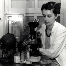 a black and white image of a woman at a microscope