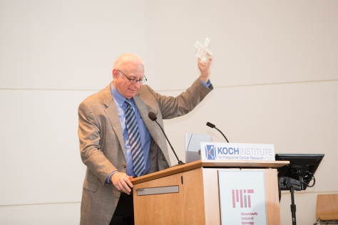 Art Gelb at a lectern holding up a small glass trophy in the shape of an X