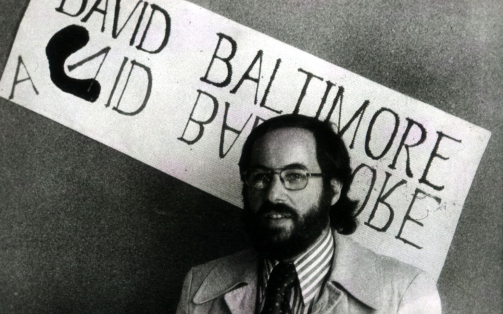 Black and white photo of David Baltimore standing in front of a sign with the text David Baltimore