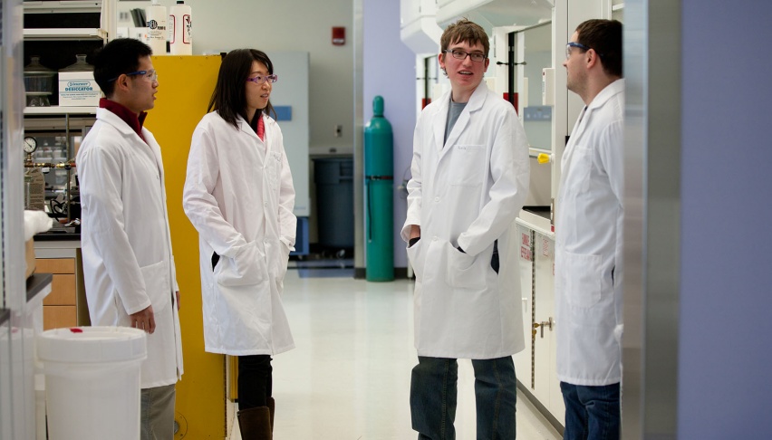 4 people in lab coats talking in a lab