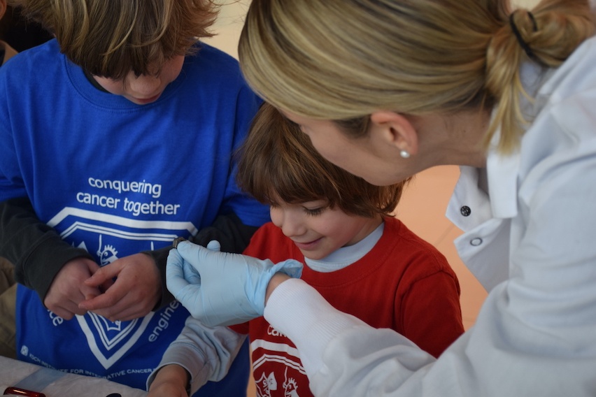 A researcher in a lab coat shows an object to two young visitors