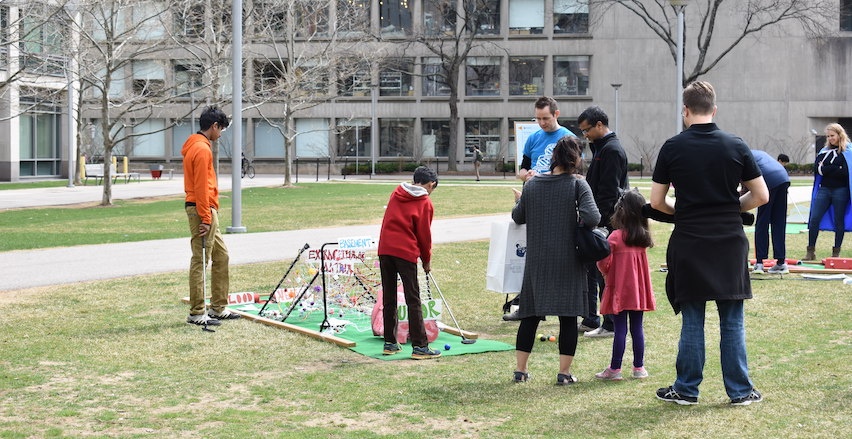 A child putts on the green while others watch