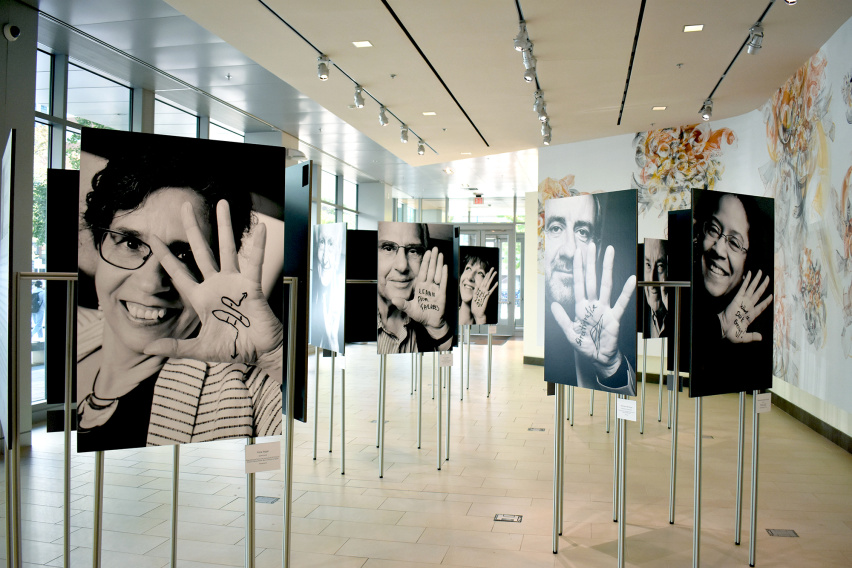 Several portraits in a gallery, picturing scientists holding their hands up with messages written on them.