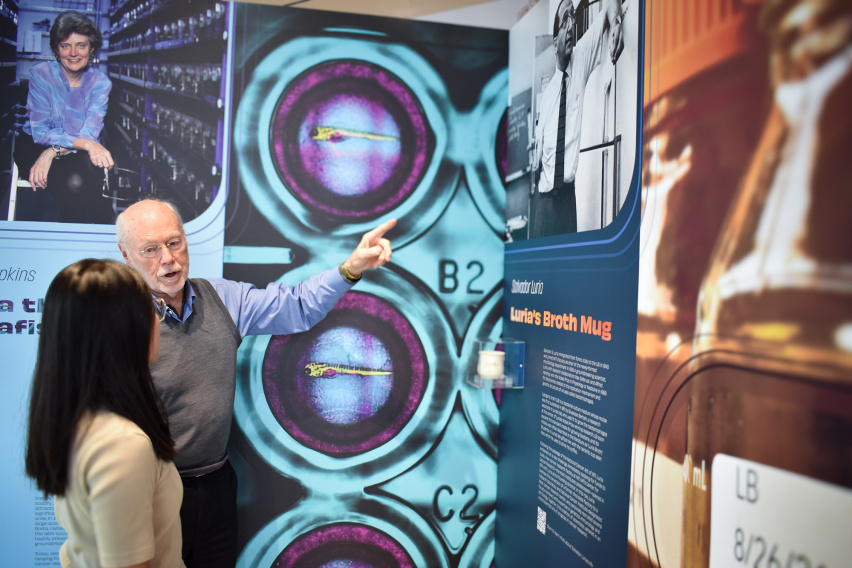 two people engage with an exhibit panel displaying a ceramic mug in an acrylic case