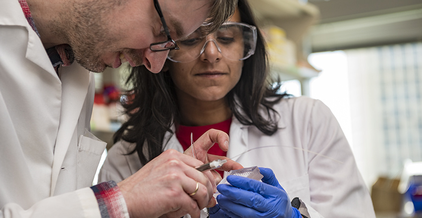 One research holds up a small device while another works on it