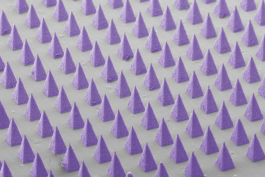 alse-colored scanning electron microscope image of dozens of microneedles arranged in a grid 