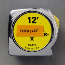 A standard 12 foot measuring tape with an orange label on it reading "Hopkins"