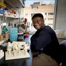 Victor Damptey sitting a lab bench with plastic models of bone joints