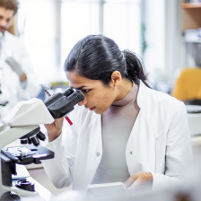 a woman in a lab coat peers into a microscope