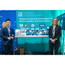 Ana Jaklenec and Jeremy Li stand in front of their exhibition booth, which includes several view screens.