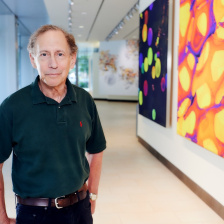 Headshot of Dr. Robert Langer, standing in front of a collection of colorful images in the Koch Institute lobby