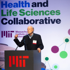 Phil Sharp stands at a podium with the text MIT Health and Life Science Collaborative behind him.