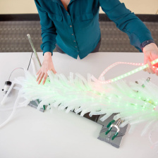 Light up cancer detection device on white table with the arms of Angela Belcher demonstrating it