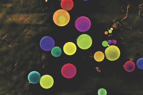falsely colored electron microscope image of spheres of various bright colors and sizes against a mottled black background 