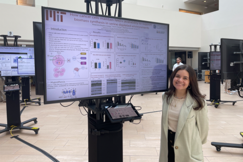 Alejandra Rosario smiling in front of a scientific poster displayed on a video screen