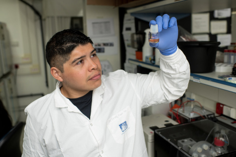 Alejandro Aguilera Castrejón in the lab holding up a small vial of red culture medium