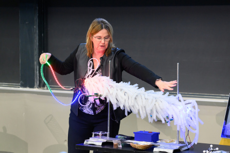 Angela Belcher demos a light-up model of M13 bacteriophage, a large tube covered in white plastic curlicues and fairy lights