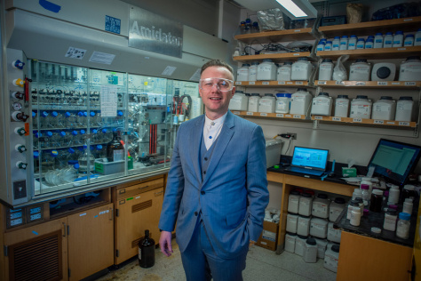 Brad Pentelute in a suit and protective eyewear, standing in his lab
