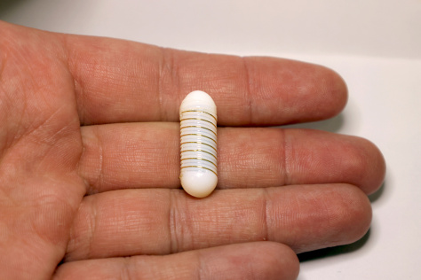 A large white, wire-wrapped capsule held in a hand