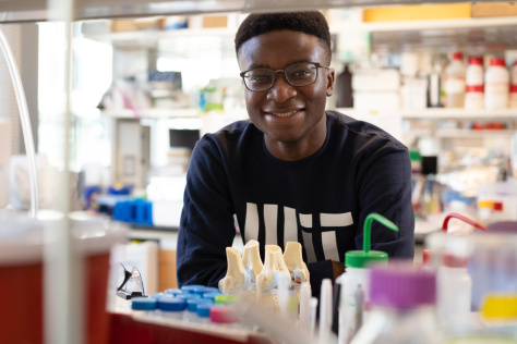 Victor Damptey wearing an MIT T shirt, leaning on a lab bench