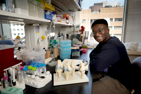 Victor Damptey sitting a lab bench with plastic models of bone joints