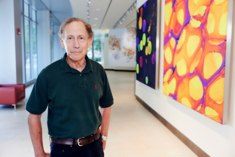 Headshot of Dr. Robert Langer, standing in front of a collection of colorful images in the Koch Institute lobby