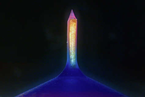 A glowing column with a gradient of pink to yellow to cyan mounted on a triangular indigo base.