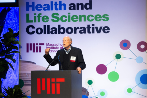 Phil Sharp stands at a podium with the text MIT Health and Life Science Collaborative behind him.