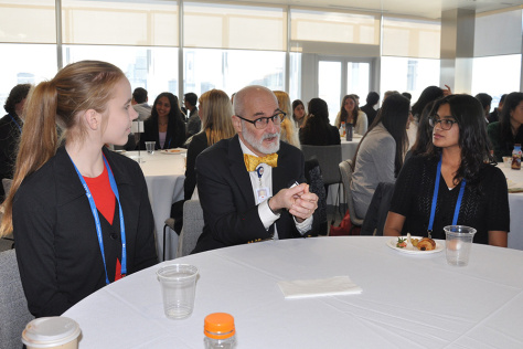 Matthew Frosch talks with two students seated at a round table bearing food and beverages.