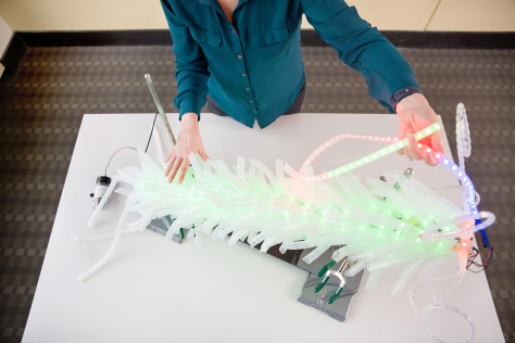 Light up cancer detection device on white table with the arms of Angela Belcher demonstrating it 