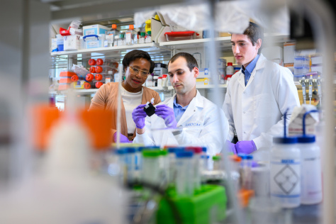 three scientists in white lab coats working in a lab