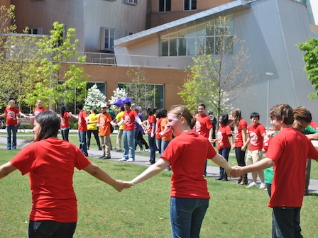 A group of students in red shirts hold hands to represent the cell membrane