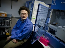 A man in a blue shirt sits next to a glass cabinet stacked with various machines.