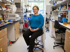 A woman sitting on a rolling chair between two lab benches.
